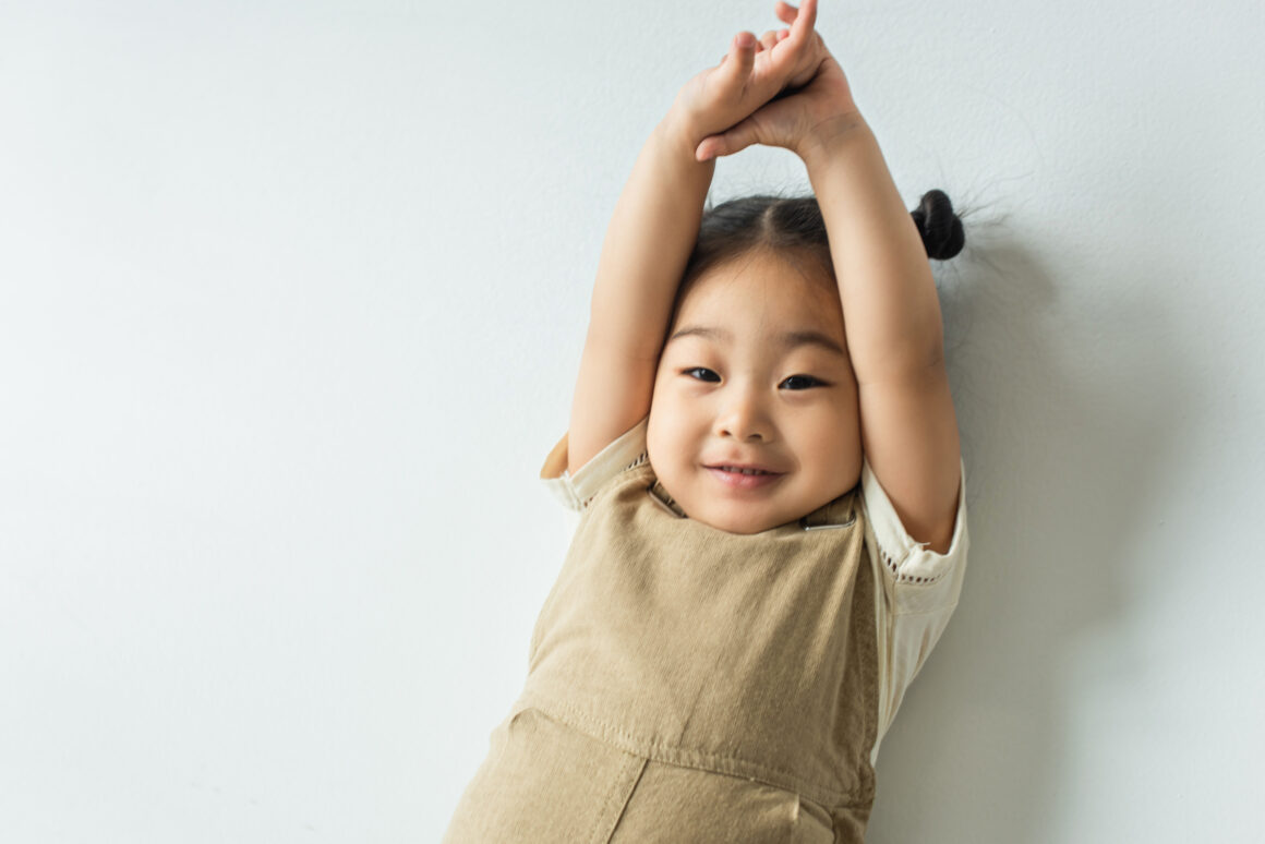 high angle view of cheerful asian toddler girl posing on grey A Guide to Choosing Comfortable and Trendy Clothes for Young Children in Singapore’s Tropical Weather